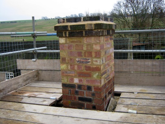 Chimney stack rebuilt to safe height above thatched roof before re-lining